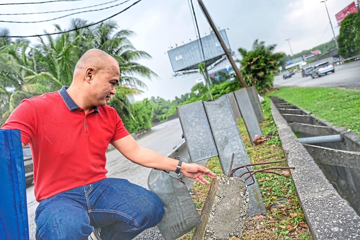 Goh showing a damaged road barrier at a Subang Jaya slip road off the Federal Highway. — RAJA FAISAL HISHAN/The Star