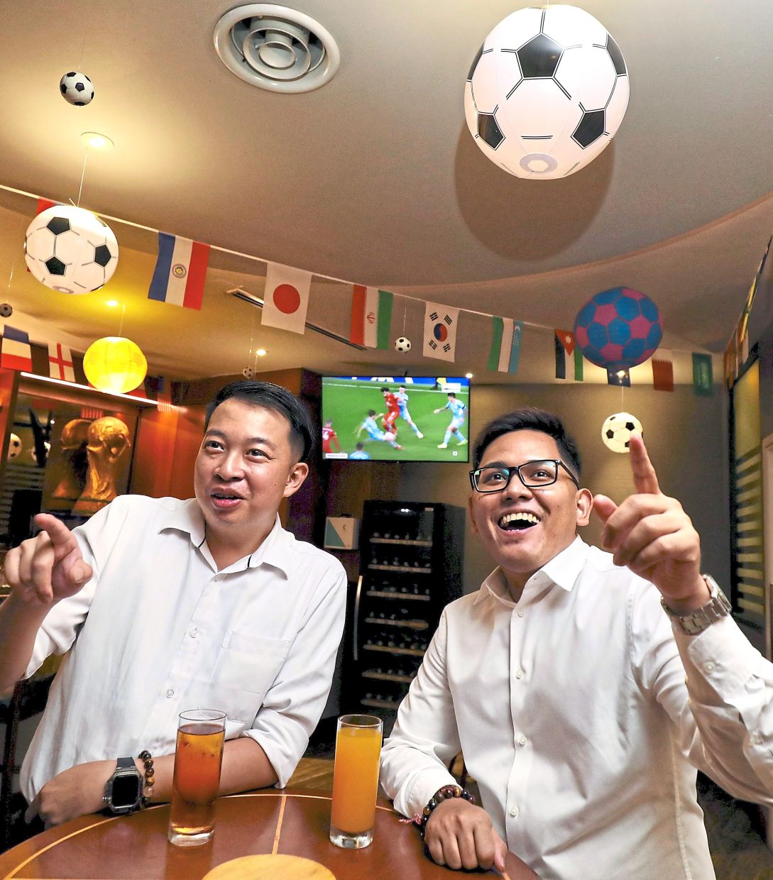 Football fever: Chan Kok Leong (left) and Visshan Miyanathan watching a football match amid World Cup-themed decorations at the lounge of Concorde Hotel Kuala Lumpur. — LEONG WAI YEE/The Star 