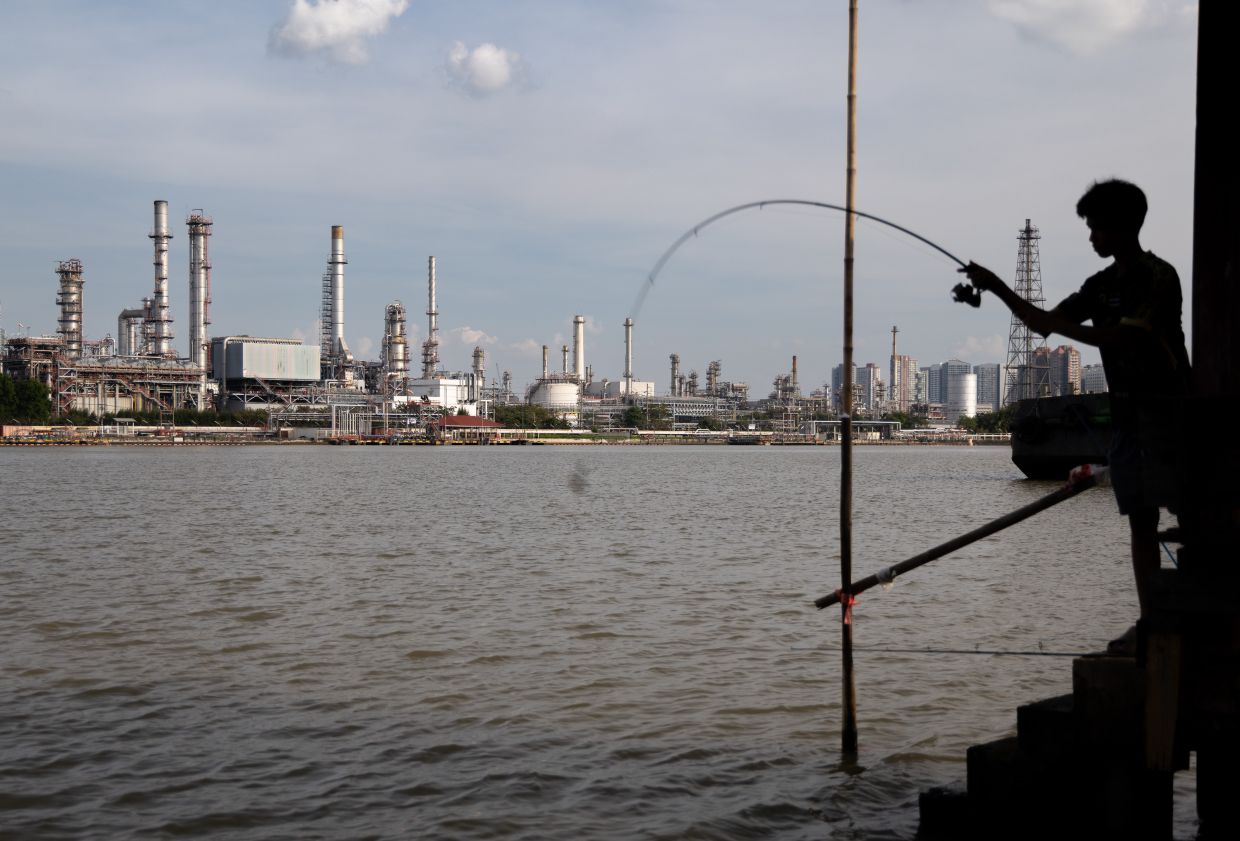 A boy fishes in front of the Bangchak Oil Refinery, home to Thailand's newest sustainable aviation fuel facility, in Bangkok. -- AP Photo/Anton L. Delgado, File