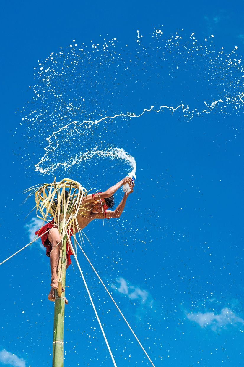 A performer climbing a bamboo pole in a traditional dance which celebrates unity, thanksgiving and cultural identity of the Bidayuh Hlibuei community. (Below) Three women from the Indonesian Bidayuh Hlibuei community are framed through their colourful beaded headgear, traditionally worn during festive celebrations such as Gawia Sowa.