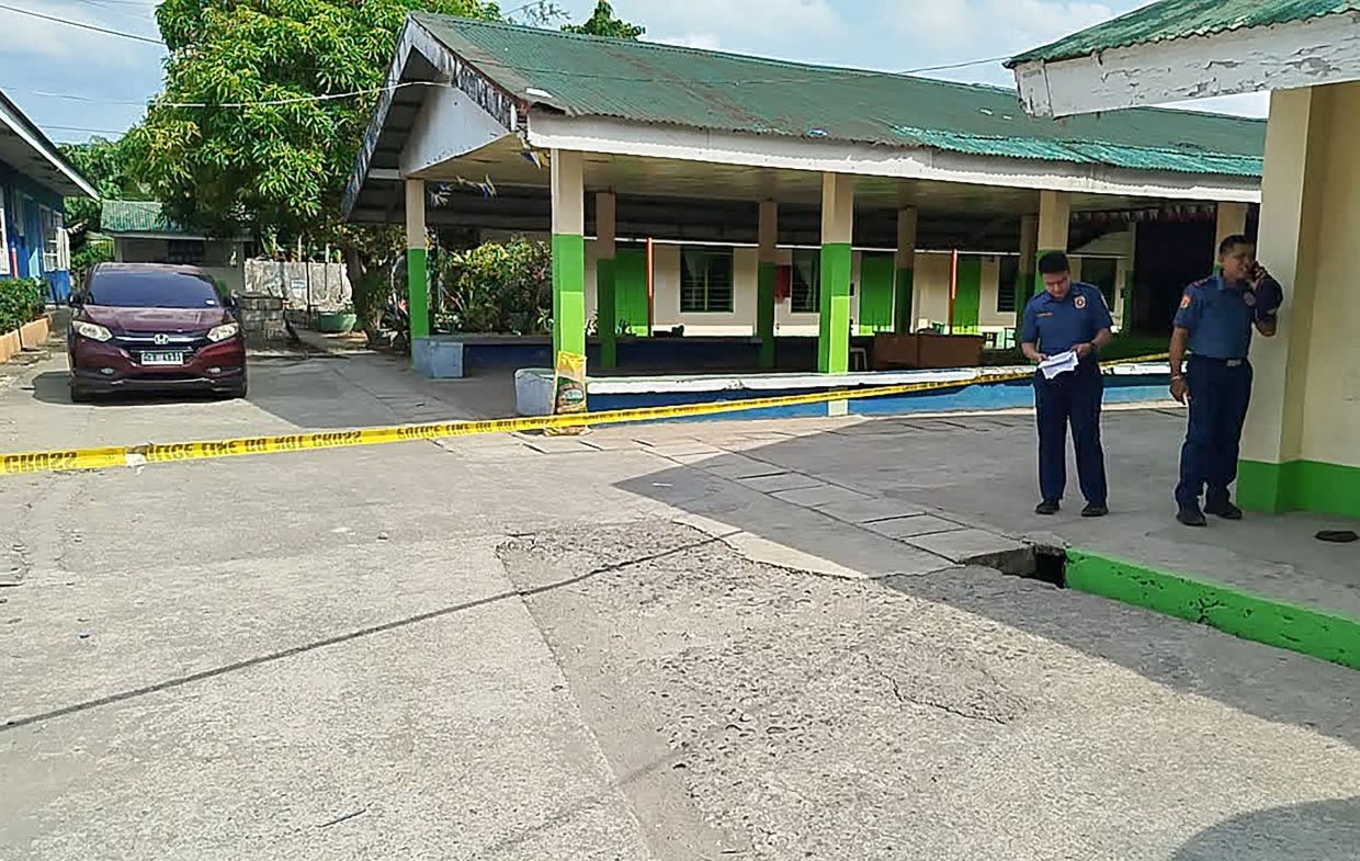 Policemen stand near the crime scene of a school compound after a shooting incident at a high school compound in Tacloban City, Leyte province, on Monday, June 22, 2026. At least three teenage students were killed and five others wounded on June 22 in a rare school shooting in the central Philippines, police said. -- Photo by NoelSianosa / AFP