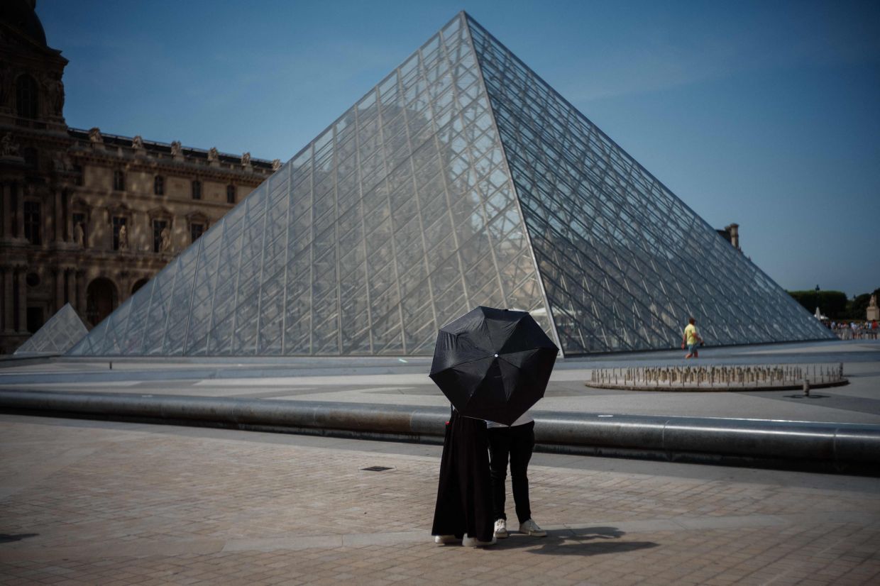 A couple in front of the Louvre Pyramid, on a particularly hot day this week. — AFP 