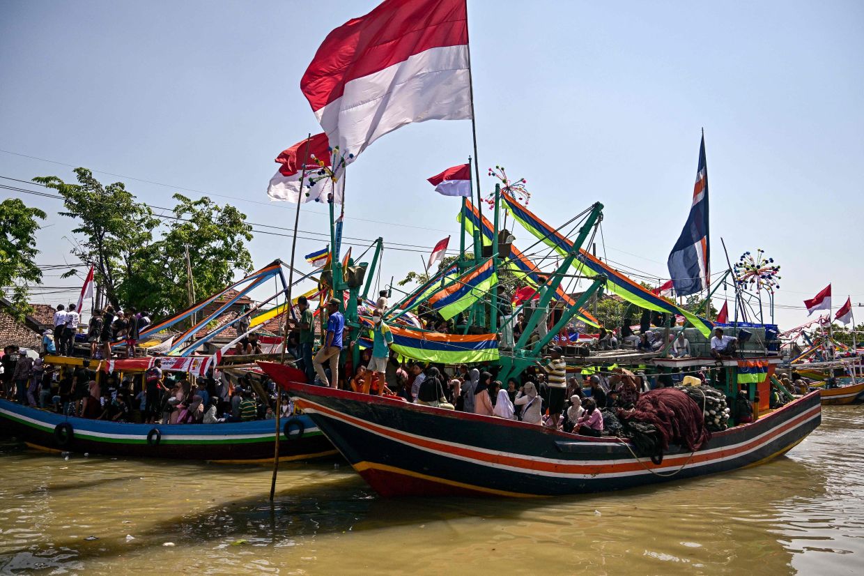 People aboard fishing boats arrive after taking part in the Petik Laut, an annual traditional Javanese thanksgiving ritual during which coastal communities express gratitude for abundant sea harvests, in Pasuruan, East Java province, on Sunday, June 28, 2026. (Photo by Juni KRISWANTO / AFP)