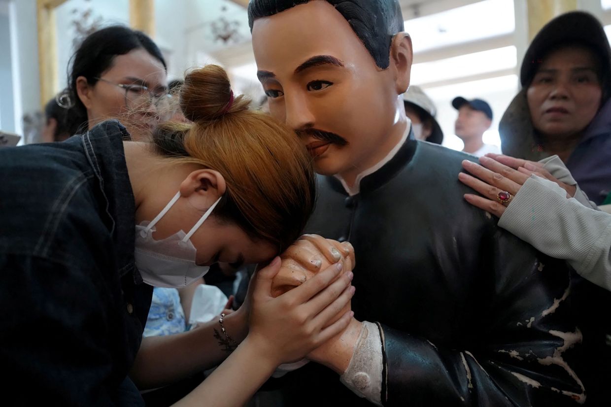 A woman holding the hand of a statue of the late priest Francis Xavier Truong Buu Diep at his beatification mass. - AFP