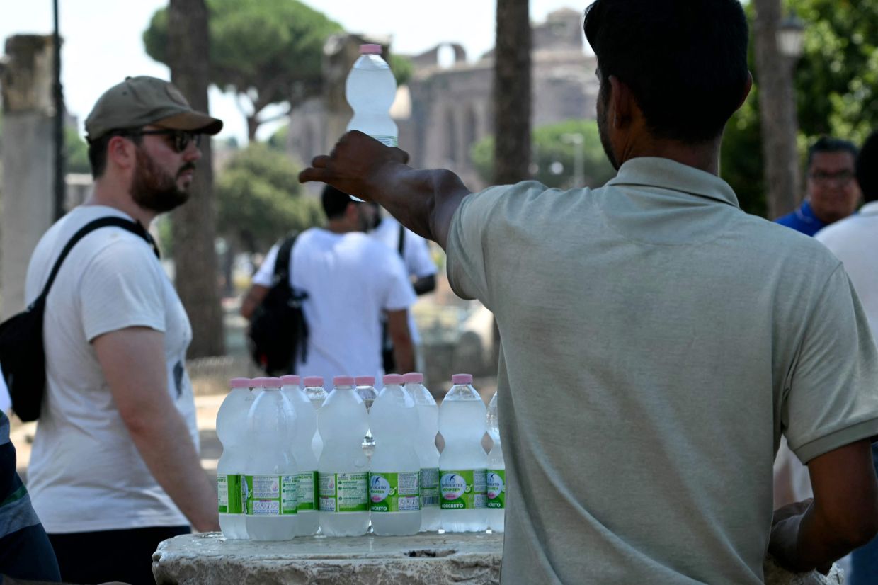 A street vendor selling bottles of water stands in the shade in central Rome during a heatwave on July 1, 2026. — AFP