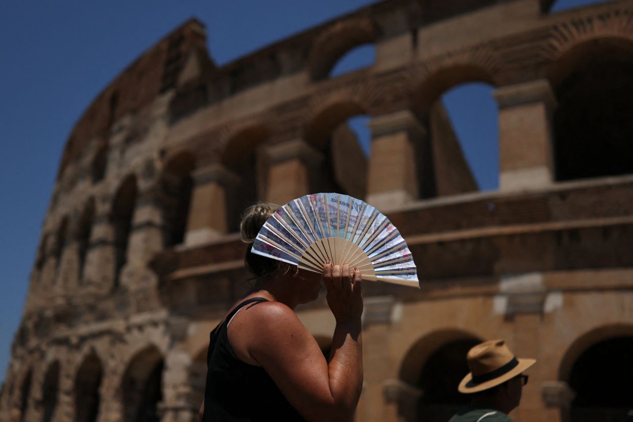 A woman uses a fan to shelter from the sun outside the Colosseum during a heatwave in Rome. — Reuters