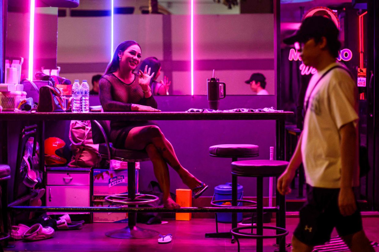 Emily (left), a sex worker, waves as she waits for clients in the back of a bar in Pattaya on July 2, 2026. Scantily dressed and wearing stiletto heels, hundreds of girls, some apparently very young, form a seedy guard of honour under the lights of Soi 6, a street in one of Pattaya's red-light districts. -- Photo by ANTHONY WALLACE / AFP