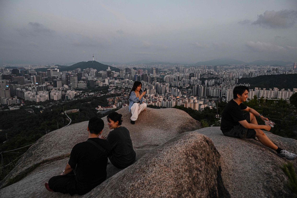 People rest on Inwangsan Mountain as the city skyline is seen in the background in Seoul on Monday, July 6, 2026. -- Photo by Jade GAO / AFP