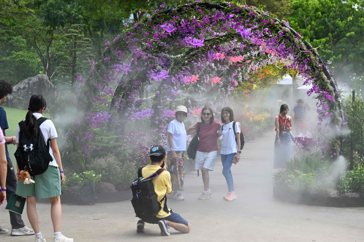 Visitors take pictures at a floral garden display as water is sprayed during the 10th Singapore Garden Festival at Gardens by the Bay in Singapore on Tuesday, July 7, 2026. -- Photo by Roslan RAHMAN / AFP