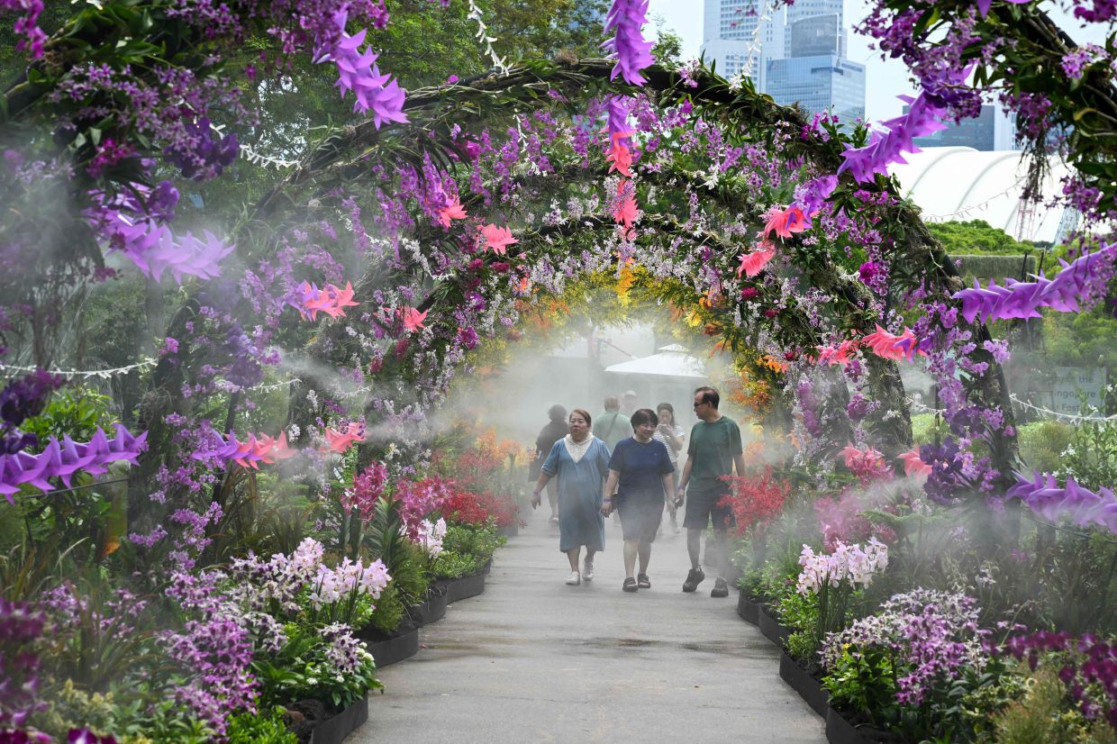 Visitors walk along the floral garden display as water is sprayed during the 10th Singapore Garden Festival at Gardens by the Bay in Singapore on Tuesday, July 7, 2026. --Photo by Roslan RAHMAN / AFP