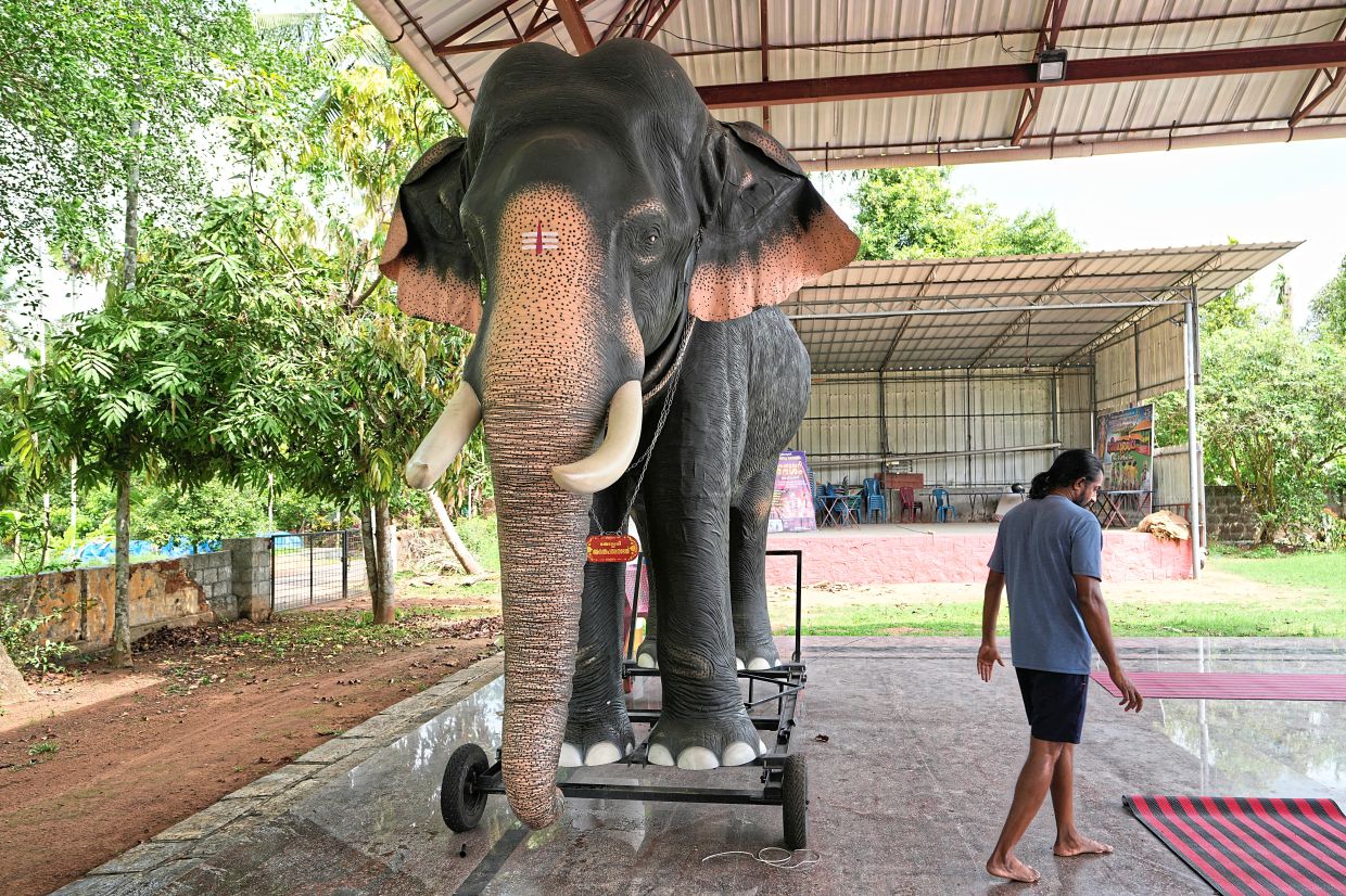 Prasanth walking past a robotic elephant manufactured by him that stands inside the compound of Cheekamundi Sri Mahavishnu Temple in Thrissur, Kerala. — AP