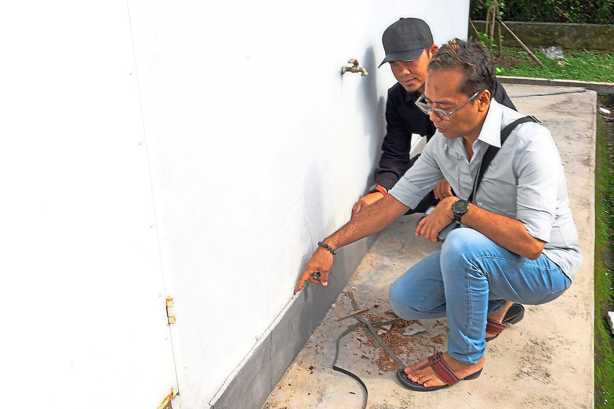 Rosli Mansor (right) showing Mohd Hafez the damage on the house’s exterior.