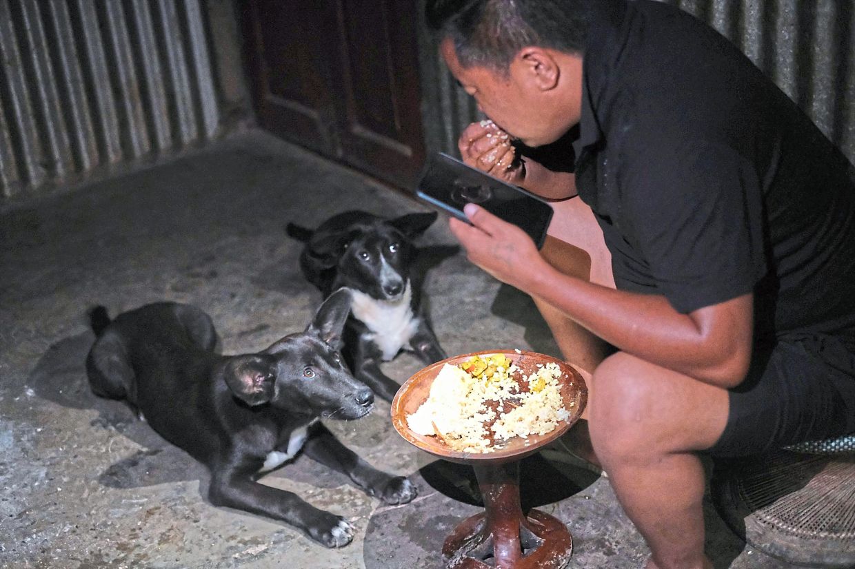 Tovi Murru, 32, eats dinner watched by his dogs inside their kitchen in Kohima, capital of the northeastern Indian state of Nagaland, Monday, July 6, 2026. (AP Photo/Yirmiyan Arthur)