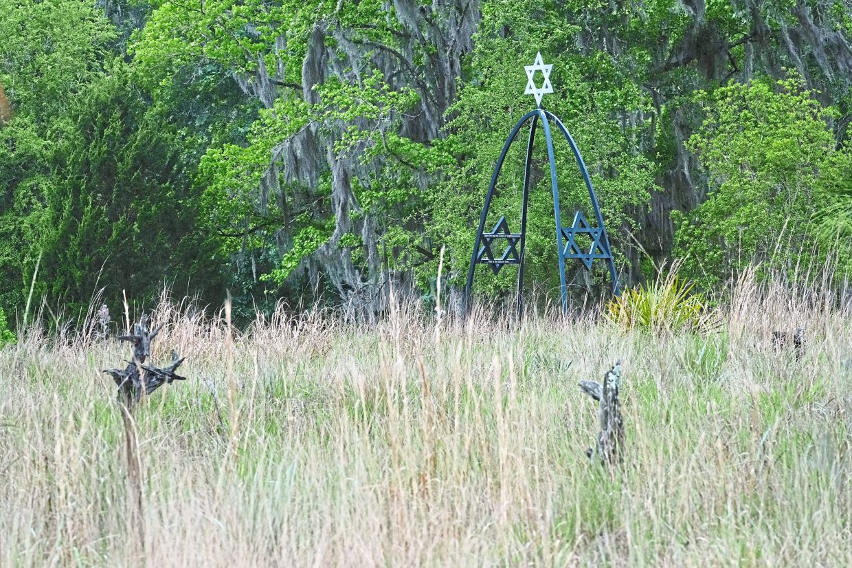 An arch leading to the Jewish burial site rises over grave markers on a field of native grasses at Prairie Creek Conservation Cemetery.