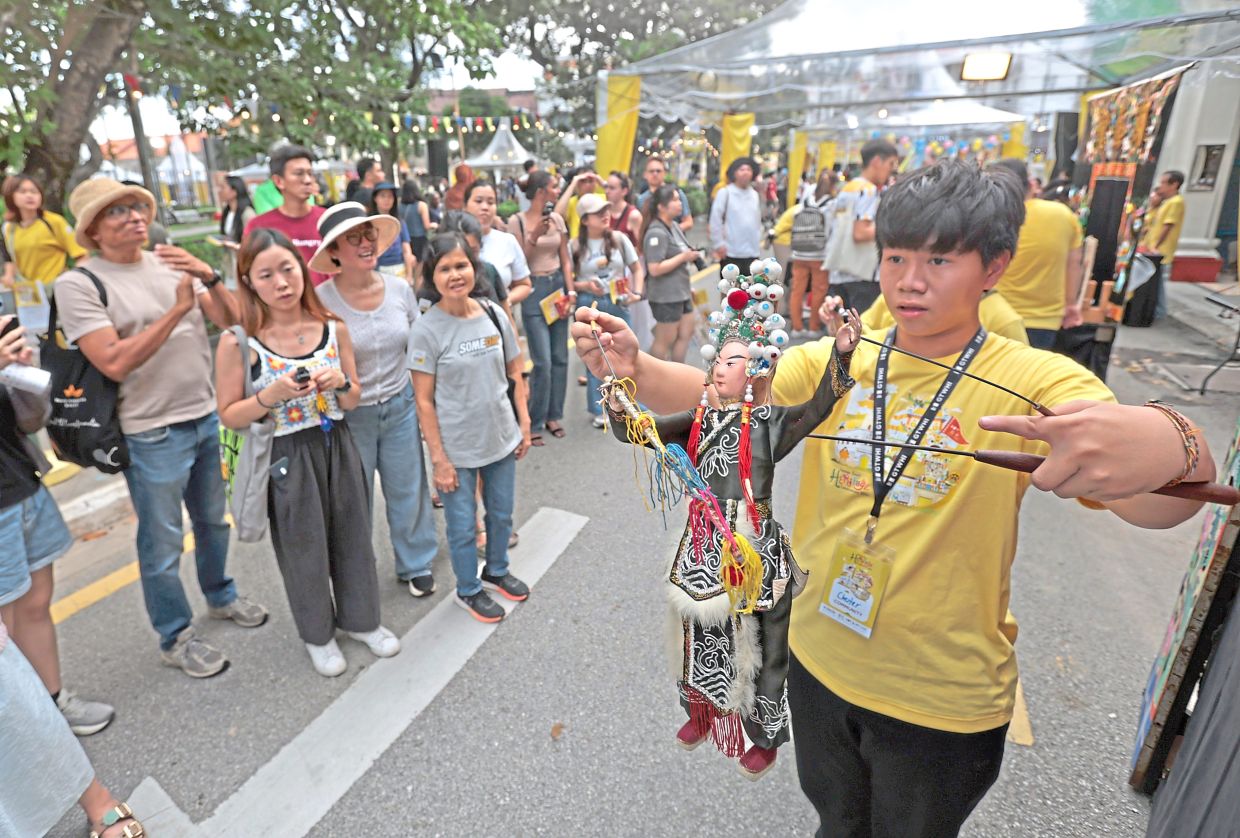 A volunteer in front of the Teochew Puppet and Opera House giving an iron-rod puppetry demonstration. 