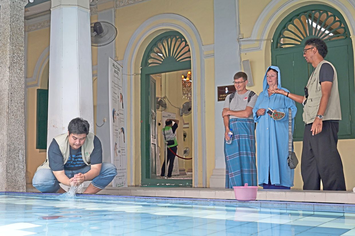A volunteer demonstrating the ablution process to tourists visiting Masjid Melayu Lebuh Acheh.