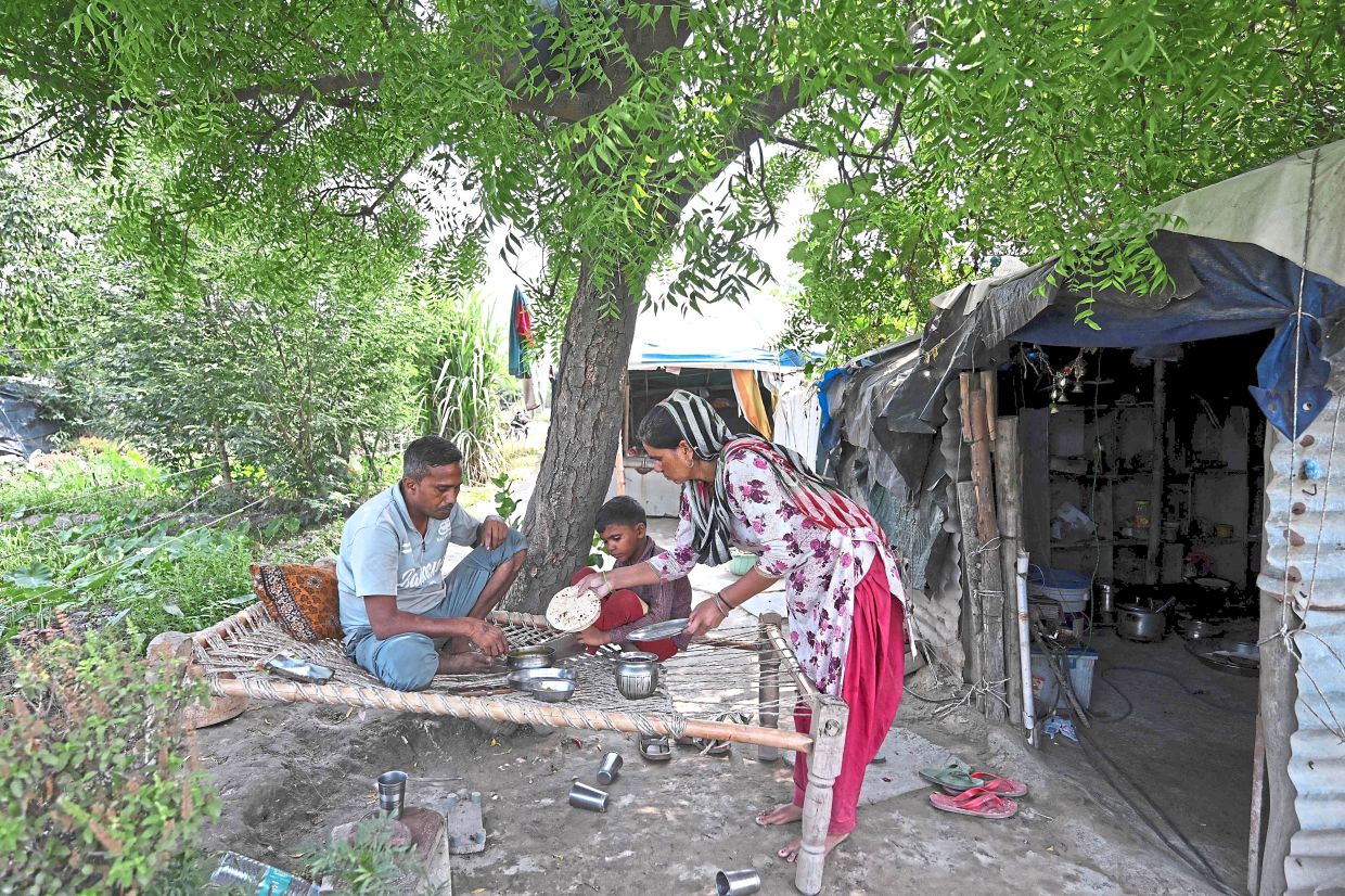 Sweltering conditions: (Above) Debvati serving lunch to her husband and son outside their shanty on the Yamuna river floodplains. — AFP/Reuters