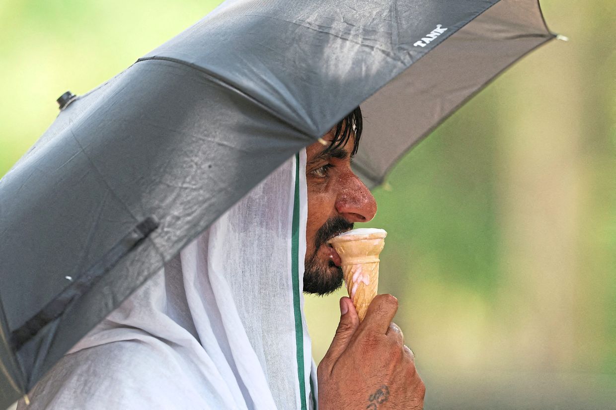 A man eating ice cream under an umbrella on a hot summer day in New Delhi. — AFP/Reuters