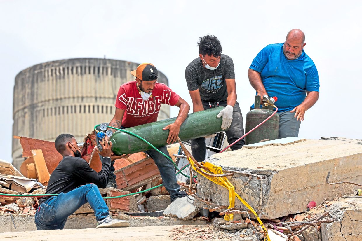 3. Residents cutting through twisted rebar as recovery efforts continue at the site of a collapsed building. — Reuters