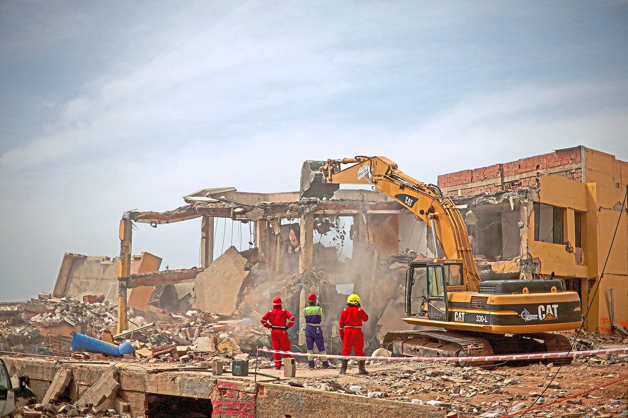 6. Rescuers watch as an excavator clears mountains of rubble from a destroyed building in the search for victims. — Reuters