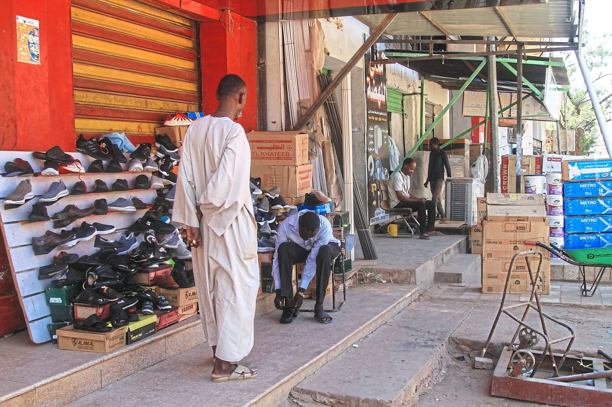 A man trying on a pair of shoes in Khartoum, and (bottom) a worker preparing masonry mortar on a street as work on rebuilding the city begins. — AFP