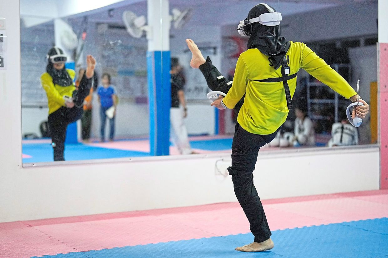 Raja Mardiah, 45, wearing a virtual reality headset, performs a high kick during a training session using an immersive VR taekwondo system in Puchong.