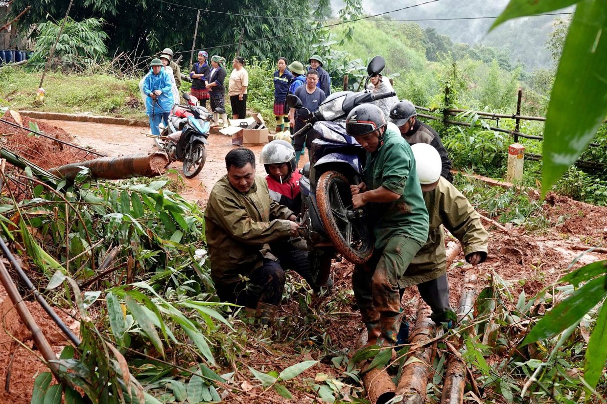 People carry a motorbike across a landslide site in Mu Cang Chai Commune in Lao Cai Province, northern Vietnam. Severe flooding and landslides caused by heavy rains killed at least four people in Vietnam, state media reported. -- Photo by A Lu / AFP