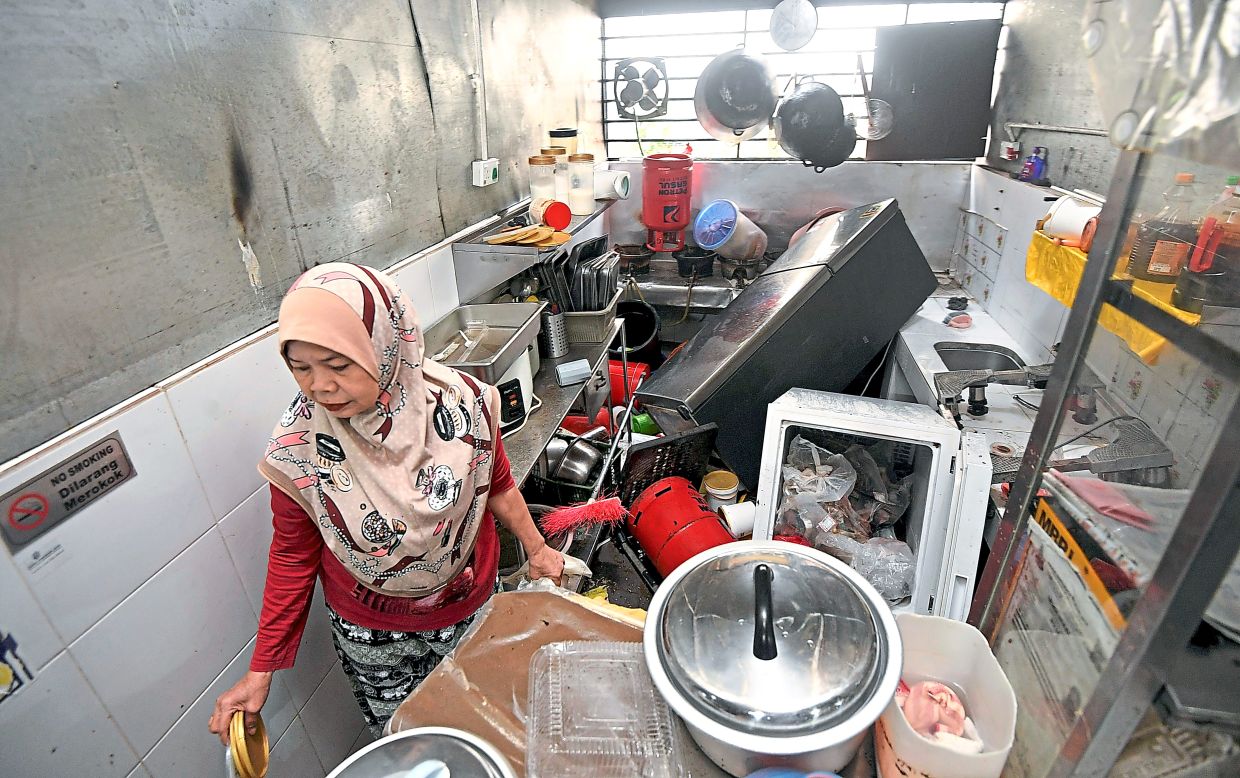Nuraini cleaning her stall after floodwaters overturned her refrigerator and scattered items.
