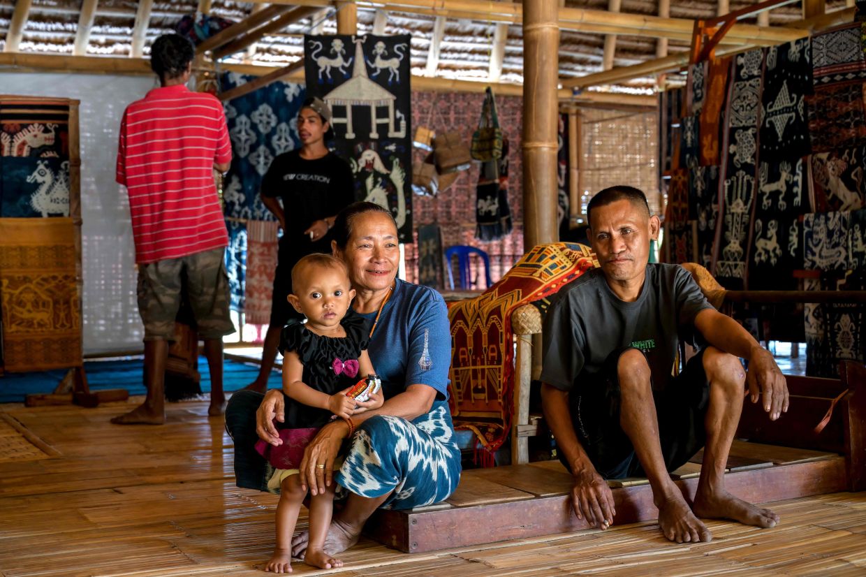 Tonda Mbitu (centre), an 'ata' (slave), sitting with family members alongside their hand-woven fabrics sold as a source of income as they receive no wages from their masters, at Kampung Raja Prailiu. - AFP
