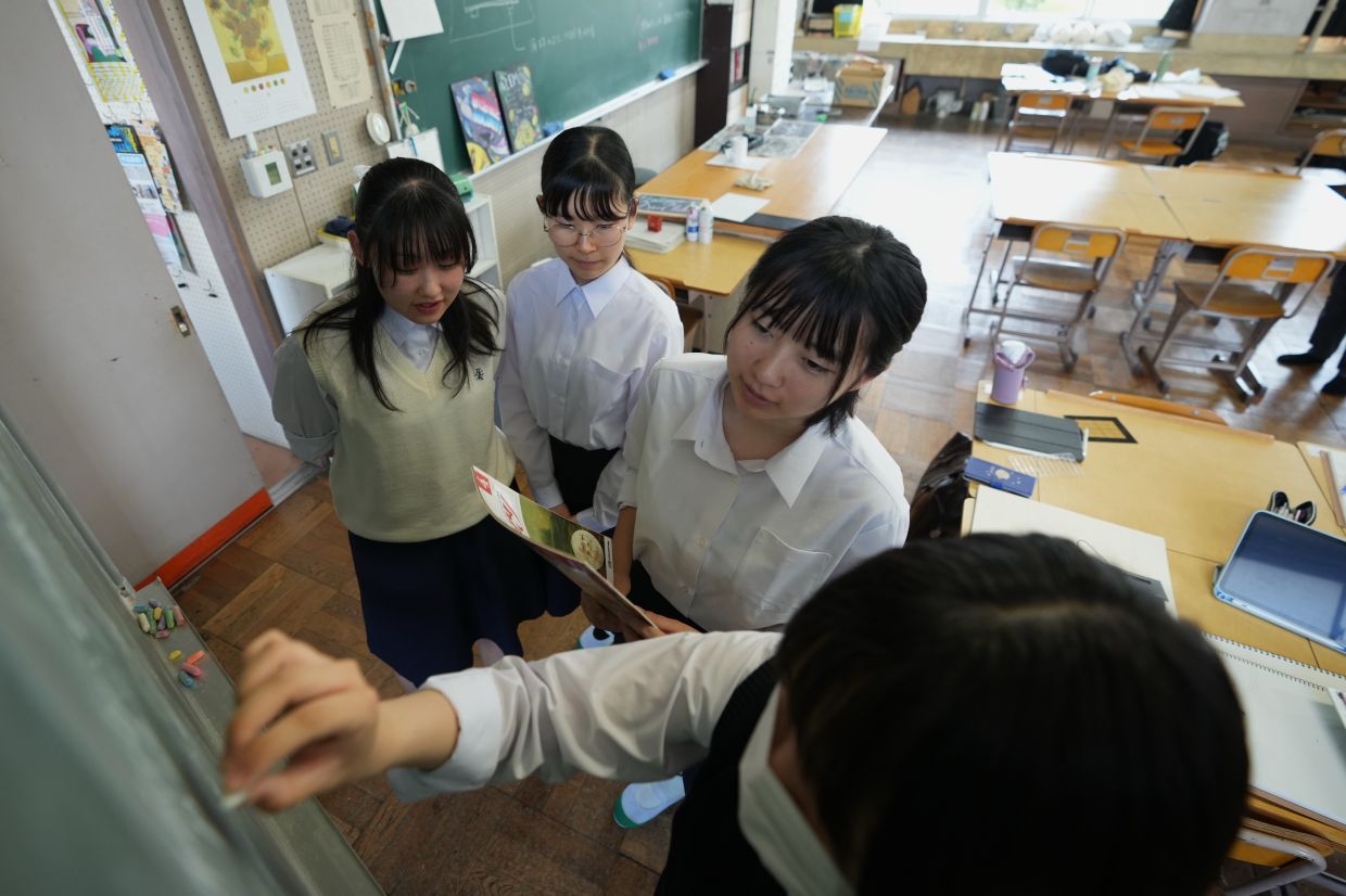 Karin Makishima, from left, Mako Kato, Chiho Ninomiya and Kanami Murata, freshman members of the art club at Kumagaya Girls High School, discuss ideas for chalk art drawing at the school in Kumagaya, northwest of Tokyo, Tuesday, July 21, 2026, as they are part of the team participating in a national blackboard art contest. (AP Photo/Hiro Komae)