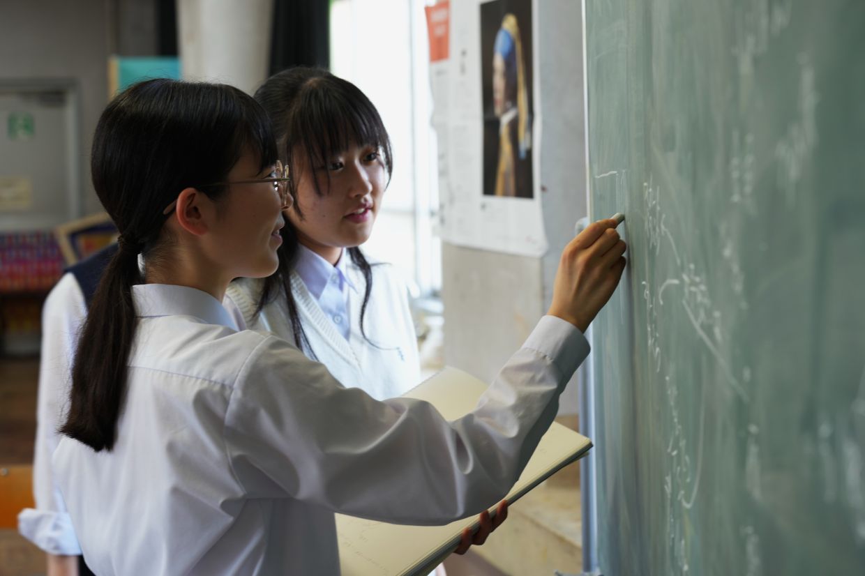 Mako Kato, left, and Karin Makishima, freshman members of the art club at Kumagaya Girls High School, discuss ideas for chalk art drawing at the school in Kumagaya, northwest of Tokyo, Tuesday, July 21, 2026, as they are part of the team participating in a national blackboard art contest. (AP Photo/Hiro Komae)