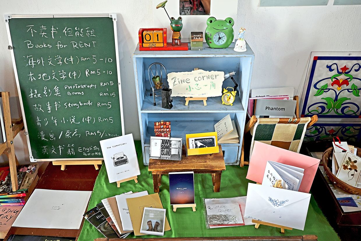 A chalkboard displays the rental prices for various book genres, next to a dedicated zine corner at Books R&R, a reading space at Lebuh China.