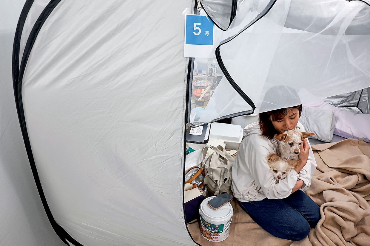 Tomoko Takaoka, who evacuated from Uki with her pet dogs Ku and Sheri, sitting in a tent at the Kyushu Animal Academy in a shelter for evacuees with pets in Kumamoto. — Kyodo News via AP/Reuters