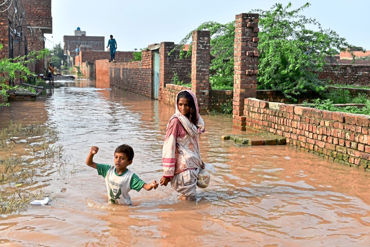 Troubled waters: A girl and a boy wading through floodwaters following monsoon rains in Ferozwala. The monsoon floods have killed over 100, displaced thousands and damaged hundred of homes. — Reuters