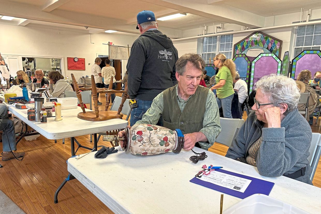 Wood repair coach Erik Hoover (left) helps someone fix a lamp.