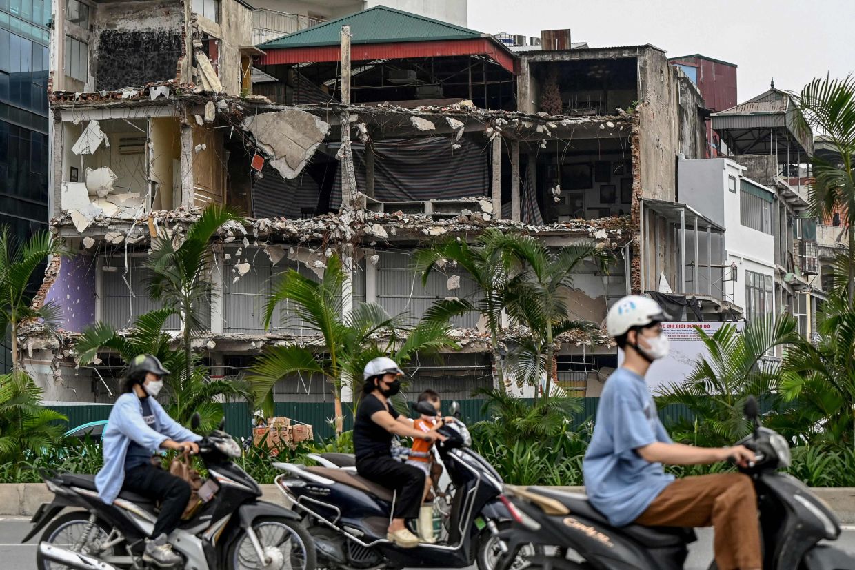 Motorcyclists commute past houses that have been demolished to widen a road in Hanoi on Tuesday, August 4, 2026. -- Photo by Nhac NGUYEN / AFP