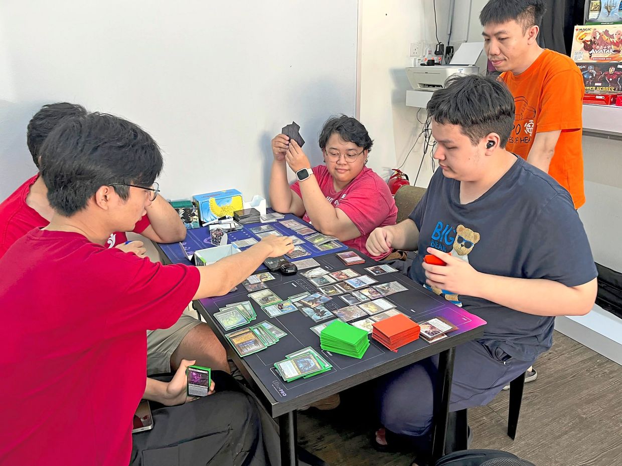 Alexandria Bookstore community members playing a competitive trading card game as Siew (standing) looks on at the shop in Jalan Nong Chik Heights, Johor Baru.