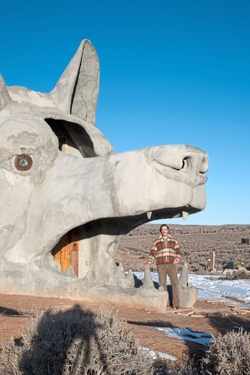 DeFeo at the entrance of the coyote-head house, where visitors enter by walking through the open maw of the creature, passing by upper and lower fangs and through a wooden front door.