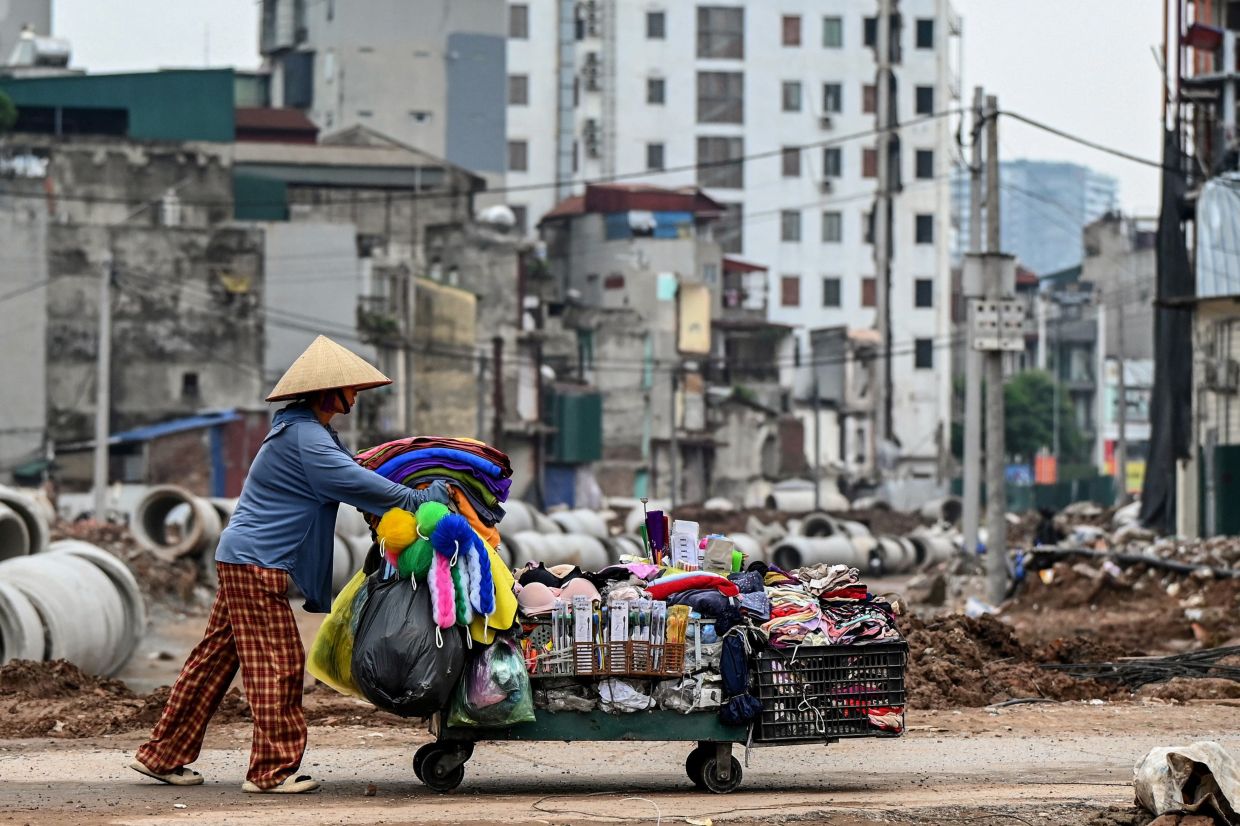 A woman pushes a cart past a road construction site in Hanoi. -- Photo by Nhac NGUYEN / AFP