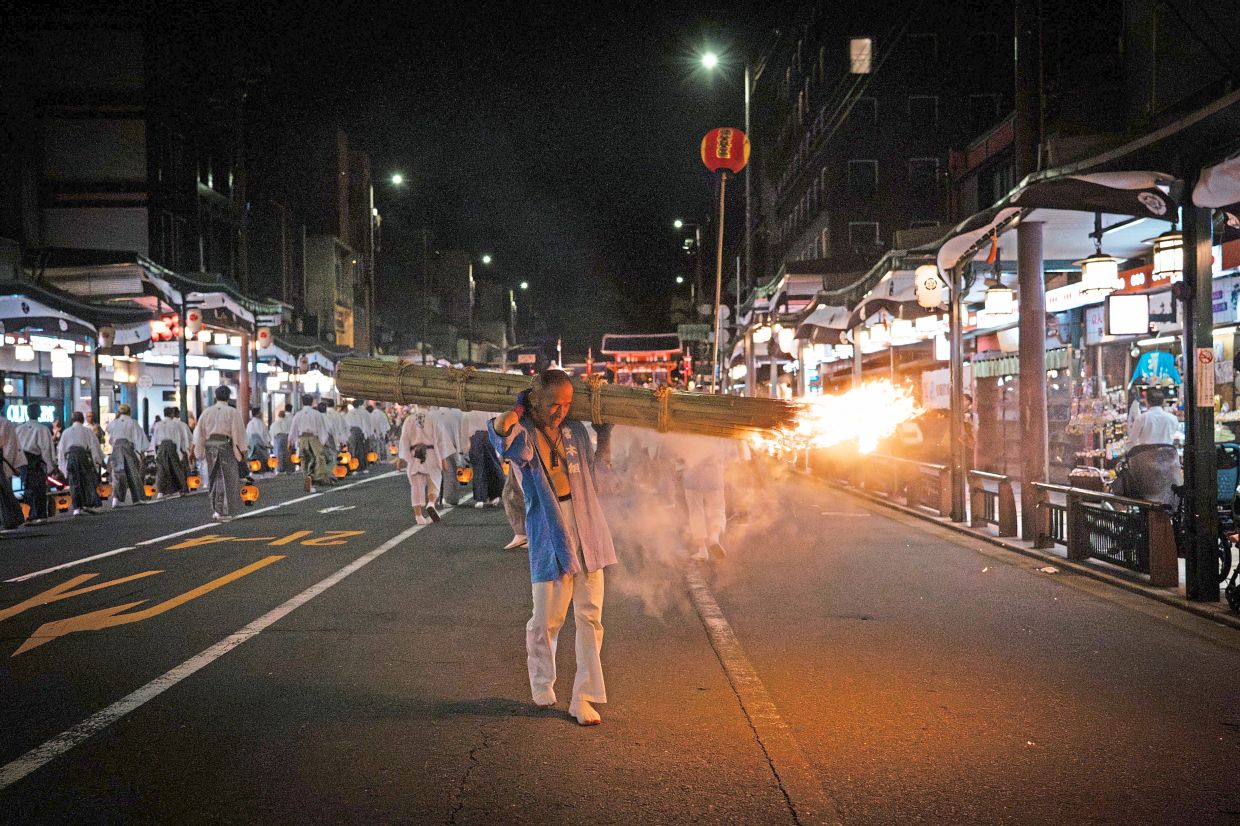 Flaming faith: A festival participant carrying a giant purification torch past tourists and local residents. — AP
