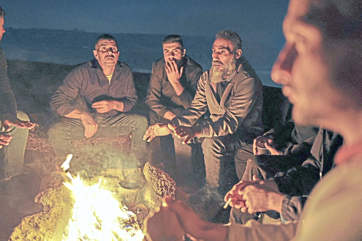 Palestinian volunteers sitting around a bonfire as they guard their town against Israeli settler attacks in Sinjil. — Reuters