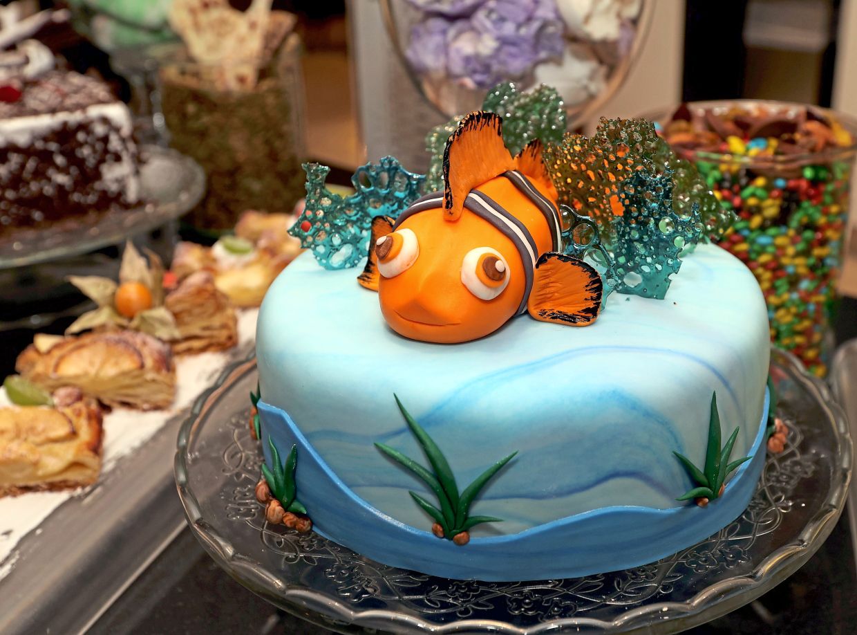 A dark chocolate cake with peanut butter cream and sugar fondant decoration of a clown fish in the dessert section.