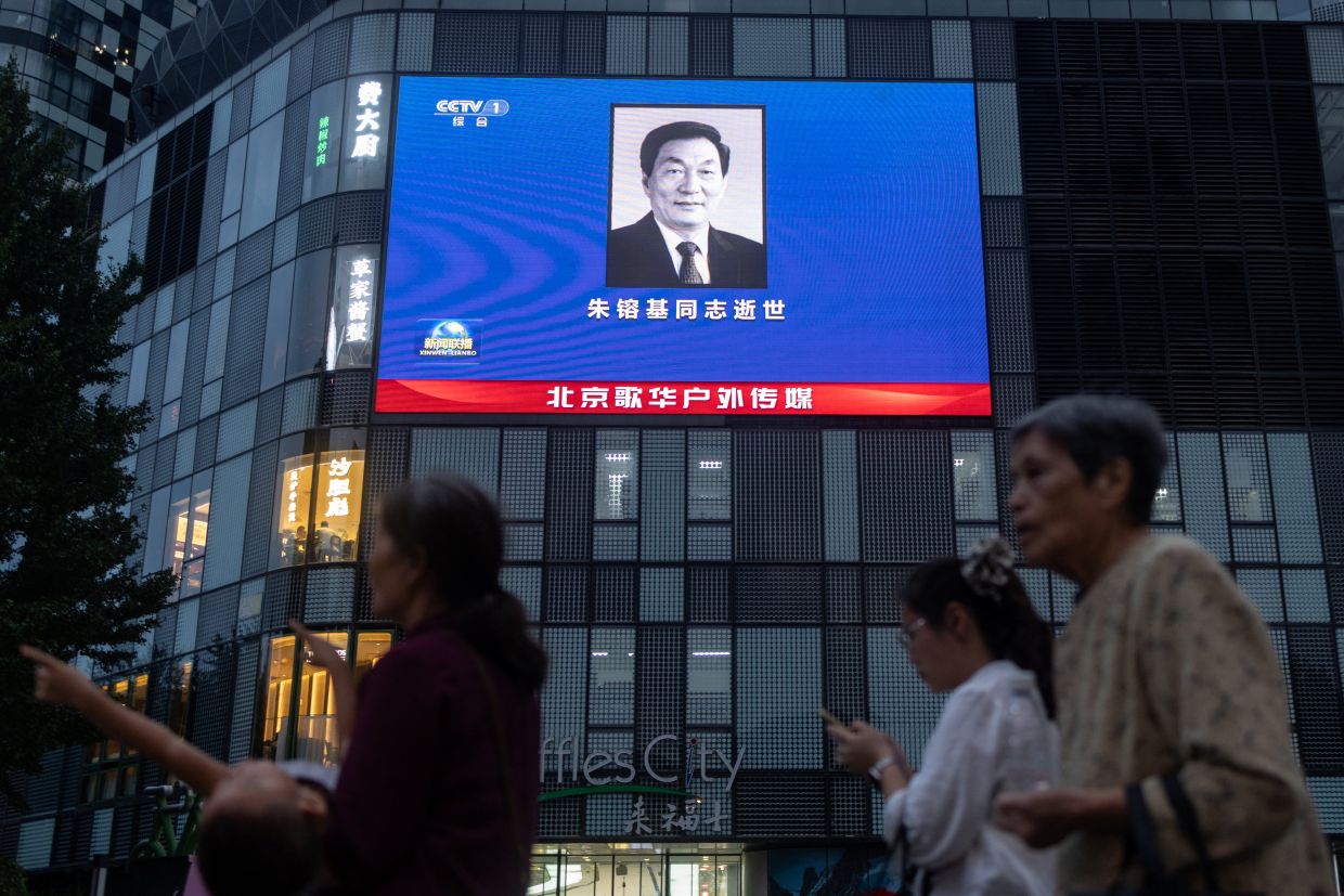 People walking next to a shopping mall featuring an advertisement screen broadcasting a portrait of former Chinese Premier Zhu Rongji who passed away on Aug 12 in Beijing. - Reuters