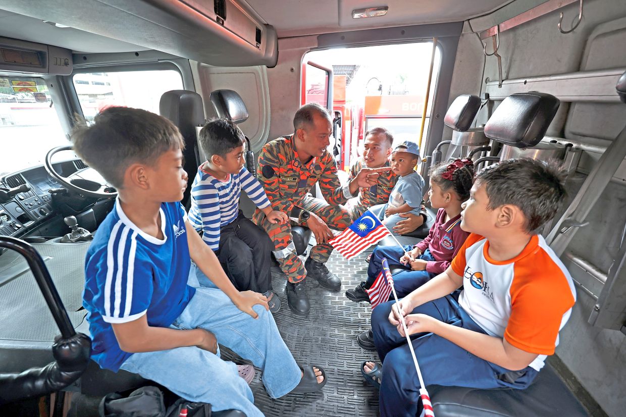 Firefighters interacting with a group of children inside the cabin of a fire engine during the programme at the Jalan Perak fire station.