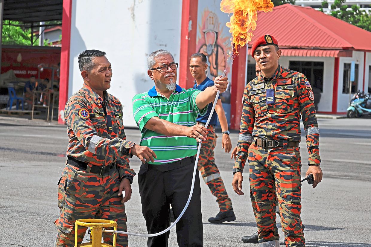 A participant learning how to safely manage a flaming cooking gas (LPG) hose under the close supervision of firefighters.