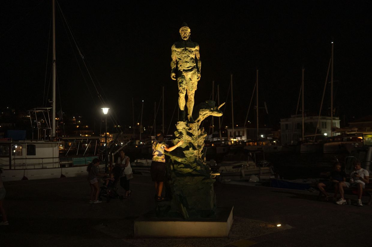 A boy stands next to a statue of Odysseus, sculpted by Korina Cassianou, in the town of Vathy on the island of Ithaca, in the Ionian Sea. Photo: AFP 