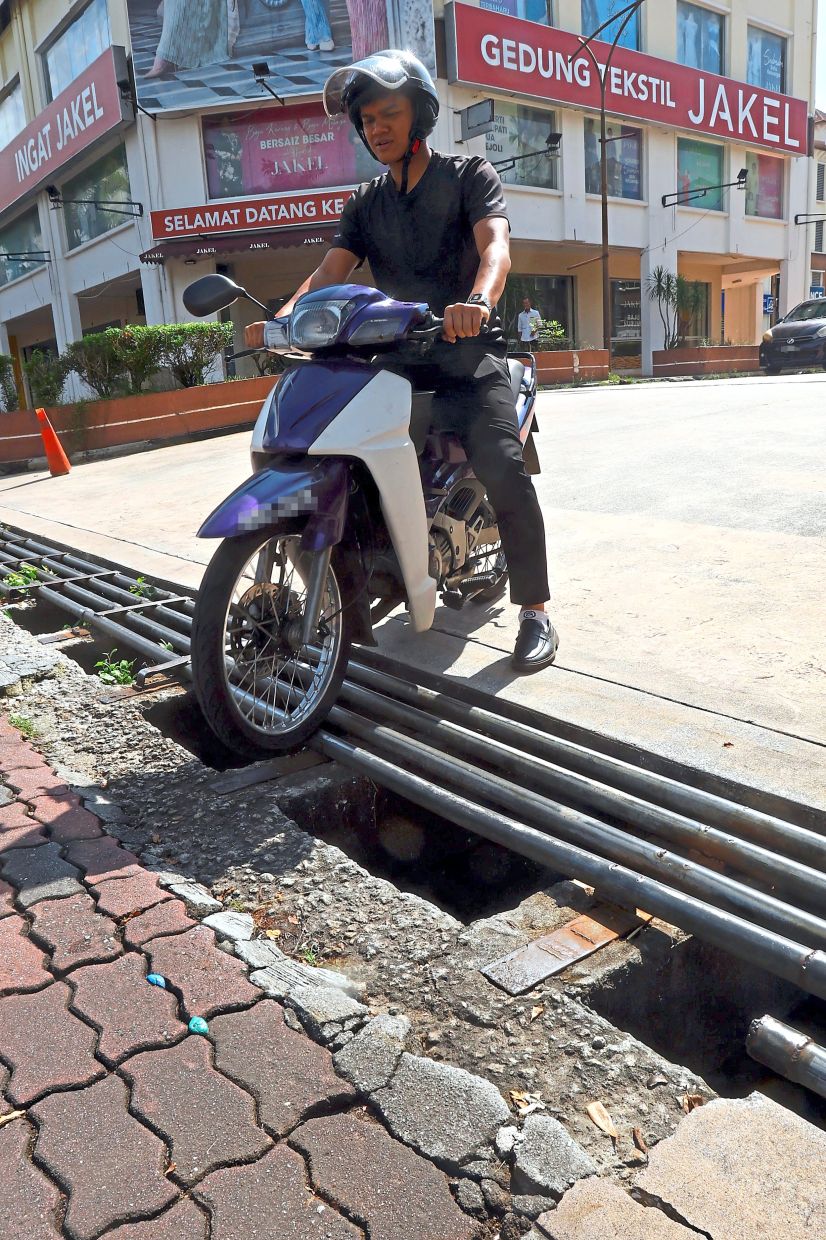 A motorcyclist carefully avoiding the gaps while riding over the deteriorating drain grilles in Greentown Avenue.