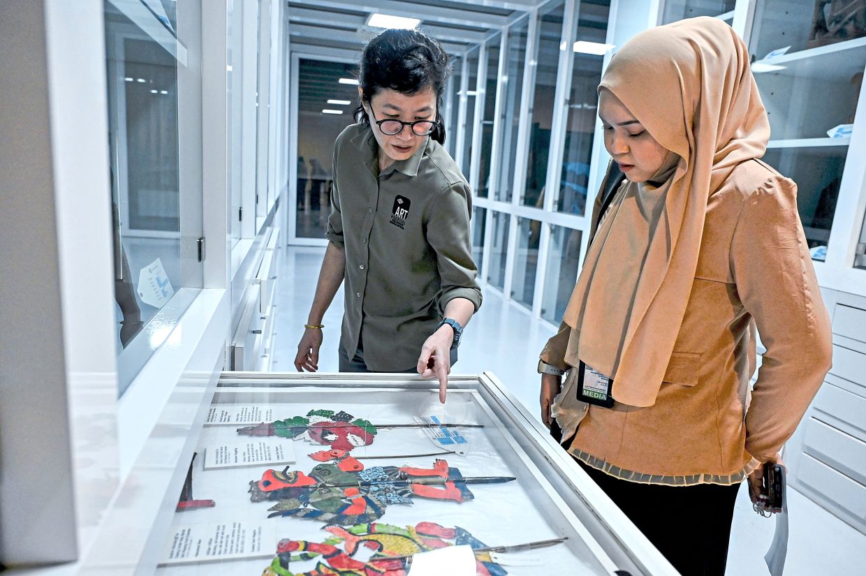 Tan (left) examines a wayang kulit figure, highlighting the conservation challenges involved in preserving traditional art forms and their fragile materials. Photo: Bernama 