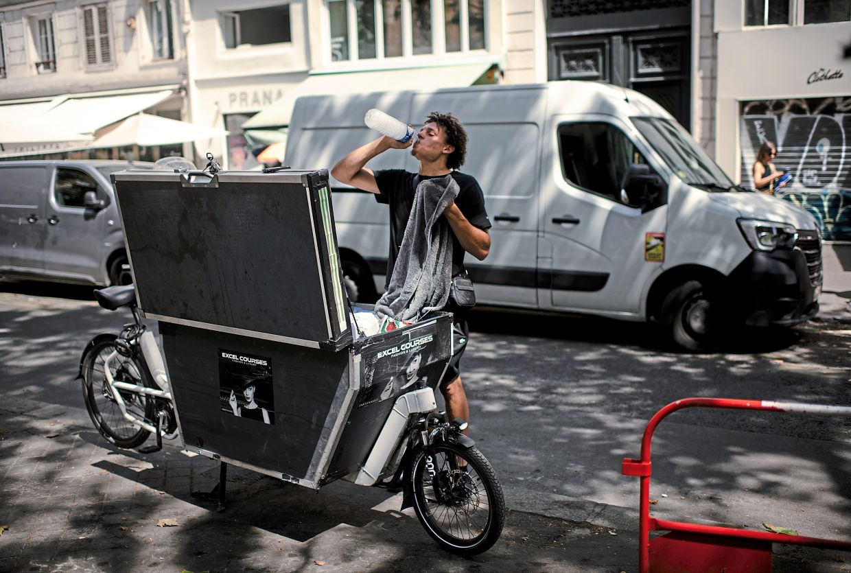 A cargo bike courier staying hydrated during a heat wave in Paris. — Dmitry Kostyukov/The New York Times