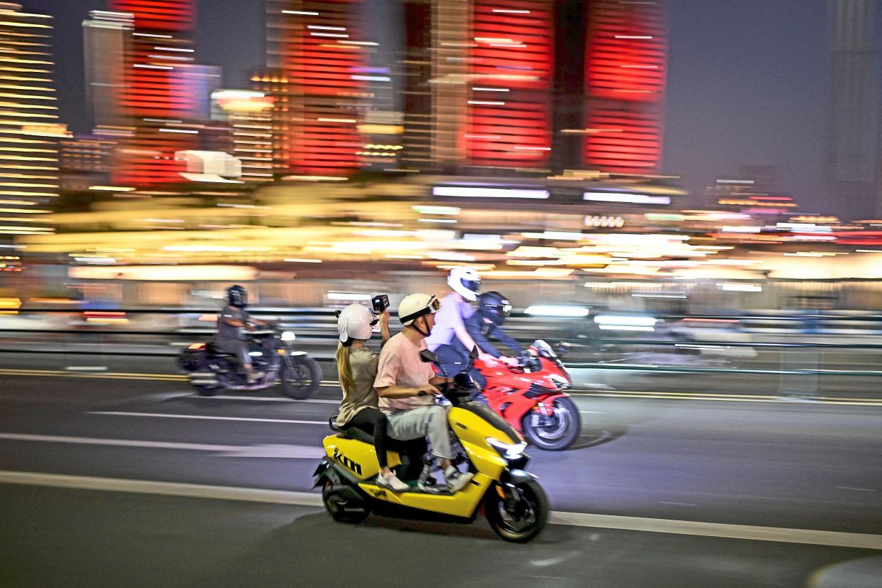 A behind-the-scenes look at how the viral motorbike videos in Chongqing are made. A woman sitting on the back of a yellow motorcycle films the scene with a mobile phone, while the client rides another motorcycle with her rider. — AFP